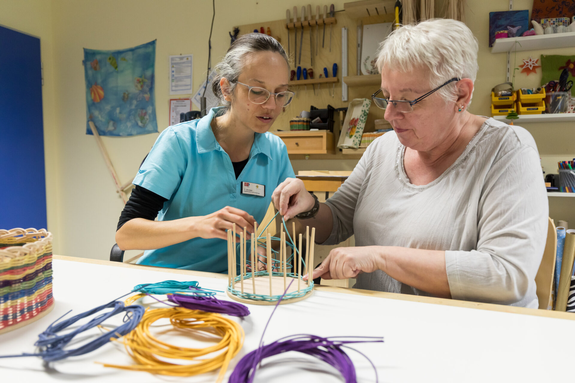 Ergotherapie: Therapeutin hilft Patientin beim Flechten eines Korbes.