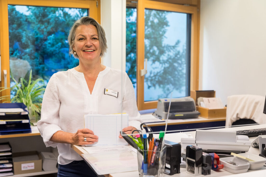 Foto am Schreibtisch der lächelnden Ambulanzsekretärin Carola Schneider der Neurologie.