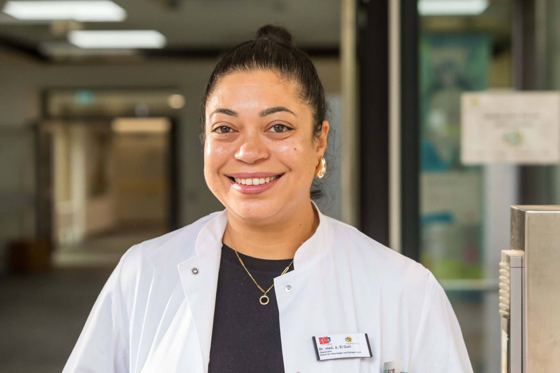Porträt der lächelnden Ärztin Afef El Ouni in weißem Arztkittel.