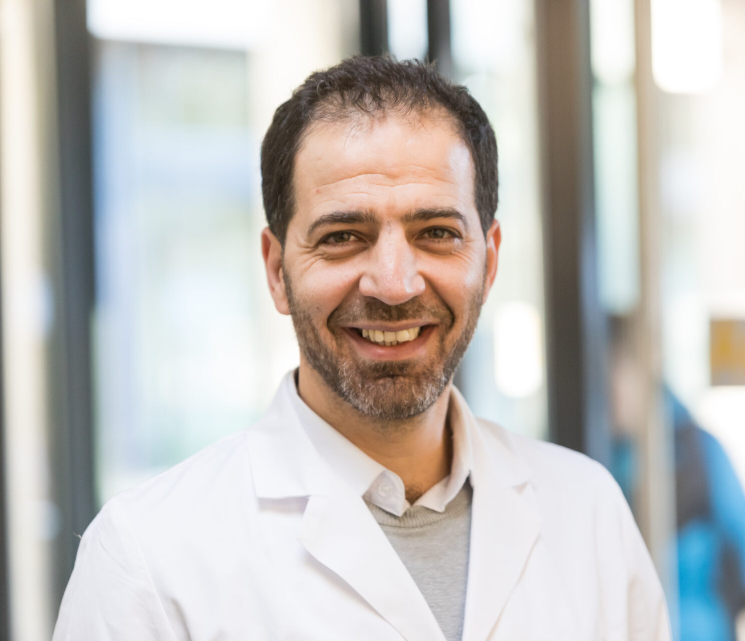 Portrait of the smiling doctor Hassan Seklawi in a white doctor's coat.