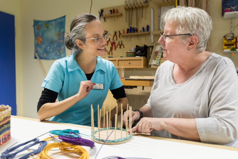 Ergotherapie: Therapeutin hilft Patientin beim Flechten eines Korbes.