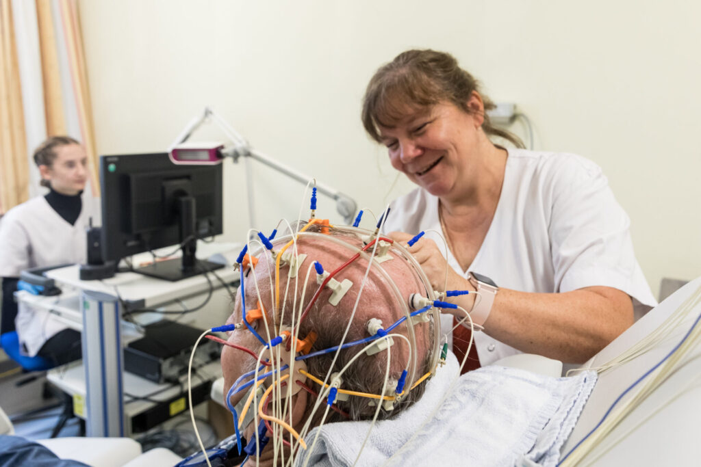 Vorbereitung zur EEG-Messung: Fachkraft befestigt Elektroden am Kopf des Patienten.