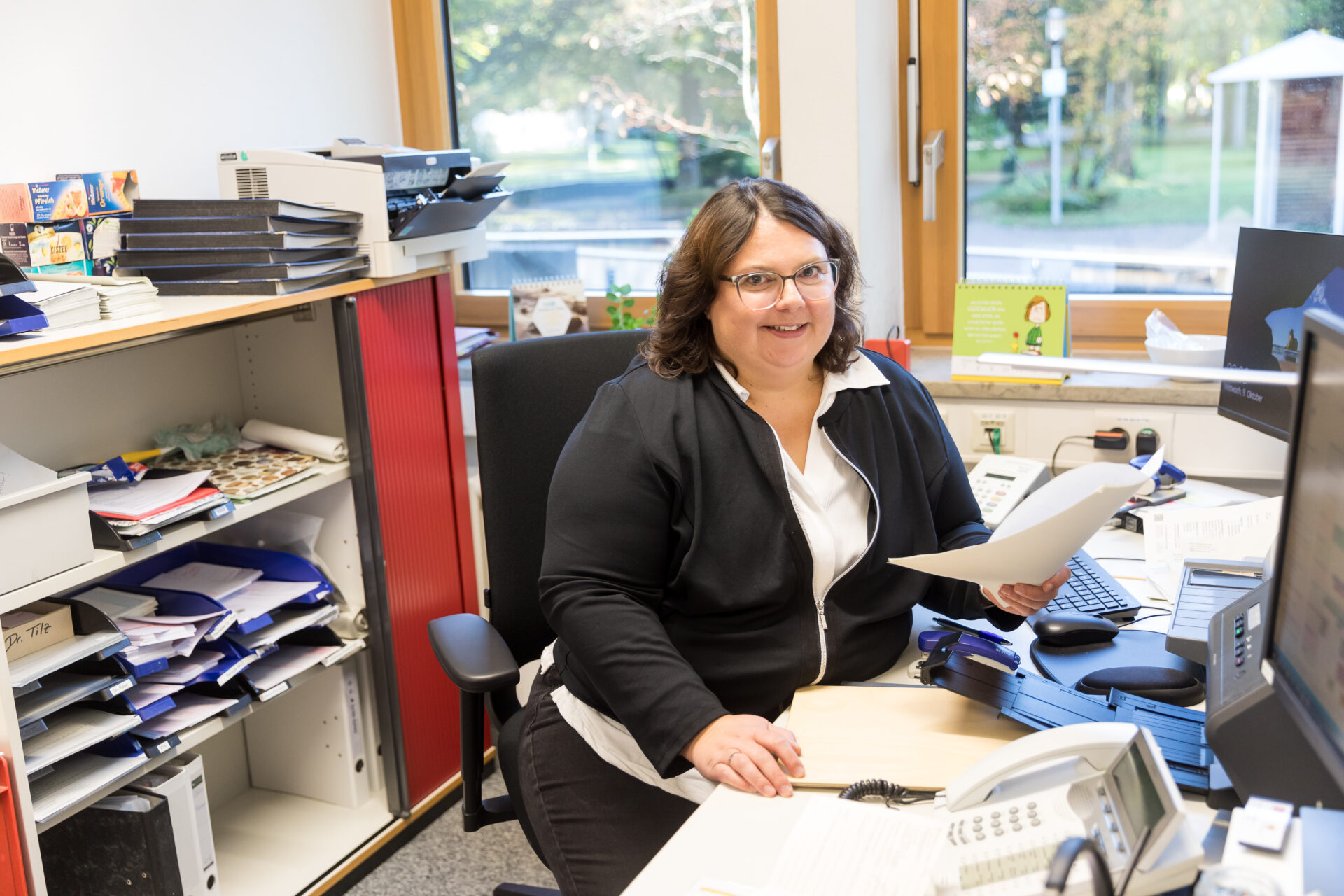 Foto am Schreibtisch der lächelnden Ambulanzsekretärin Astrid Moosmann der Epileptologie.